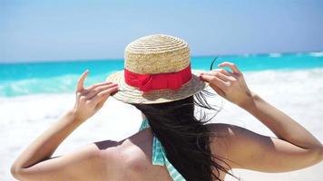 Back view of beautiful woman in hat on summer holidays on white beach. video