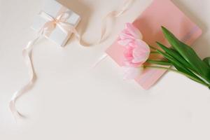 un ramo de flores de hermosa tulipanes y un regalo en un beige antecedentes parte superior vista. de la madre día fondo, enamorado día, internacional De las mujeres día. día festivo, dar un regalo. foto