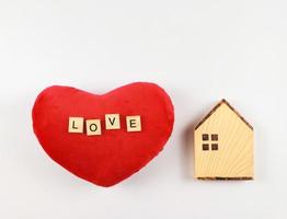 flat layout of wooden model house and red heart shape pillow with wooden letters L O V E  isolated  on white background with copy space, valentines or home of love concept. photo