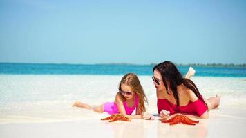 peu adorable fille et Jeune mère à tropical plage mensonge sur blanc plage et prendre plaisir leur été vacances video