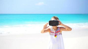 Adorable little girl using VR virtual reality goggles on the white beach. video