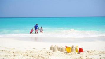 Sandcastle at white beach with plastic kids toys and family in the sea background video