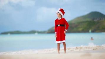 adorable chica con sombrero de navidad en la playa blanca durante las vacaciones de navidad video