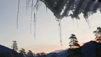 de cerca. congelado carámbanos en el borde de el techo en el antecedentes de un montaña paisaje en el noche. invierno tiempo. lento movimiento. video