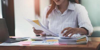 Business Documents concept  Employee woman hands working in Stacks paper files for searching and checking unfinished document achieves on folders papers at busy work desk office. Soft focus photo