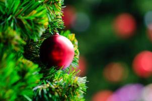 Red bauble hanging on Christmas tree with bokeh background from another bigger Christmas tree. photo