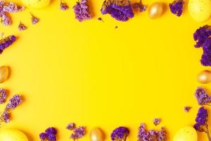 Easter yellow eggs with purple flowers on yellow background. Flat lay, copy space. photo