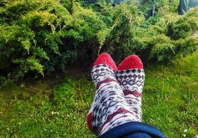 The concept of outdoor recreation, hygge and leisure - legs in woolen socks on a blurred background of green grass and junipers. photo
