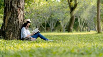 un hermosa asiático mujer disfrutando y relajarse desde leyendo libro en el parque.concepto de recreación, educación y estudiar , curiosidad, ocio hora foto