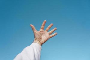 mano arriba en el aire gesticulando en el cielo azul, fondo azul foto