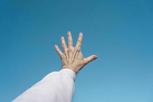 mano arriba en el aire gesticulando en el cielo azul, fondo azul foto