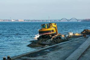 Excavator works to strengthen the embankment. Hydraulic excavator working on the river bank. photo