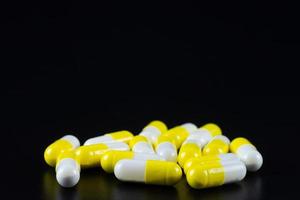 White tablet with two pills in background. Black background with reflection photo