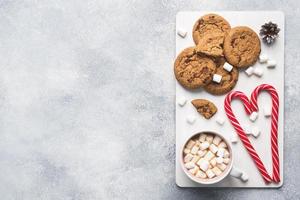 The chocolate chip cookie, Christmas cane caramel Cup cocoa and marshmallow cones Decorations on a gray background. Copy space Frame. photo