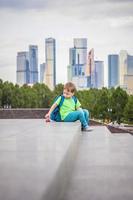 A boy is playing with a toy, sitting on the steps in the open air against the backdrop of skyscrapers and high-rise buildings. Journey. Lifestyle in the city. photo