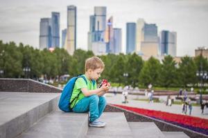 A boy is playing with a toy, sitting on the steps in the open air against the backdrop of skyscrapers and high-rise buildings. Journey. Lifestyle in the city. photo