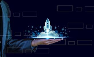 Startup business concept. Businessman holding a tablet, rocket launching and soar flying out from screen, starting a business, growing business, modern technology, hologram, network connection. photo
