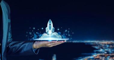 Startup business concept. Businessman holding a tablet, rocket launching and soar flying out from screen, starting a business, growing business, modern technology, hologram, network connection. photo