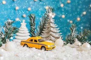 fondo de la bandera de navidad. modelo de taxi de coche de juguete amarillo y adornos de invierno sobre fondo azul con nieve. concepto de servicio de taxi de entrega de tráfico de la ciudad. foto