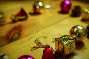 New Year and Christmas gift themed decorations on wooden background, consisting of a golden gift box.  shiny colored balls  Dried pine cones and small bells  free space for design photo