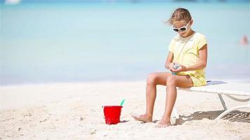 niña pequeña con una botella de crema solar sentada en una playa tropical video