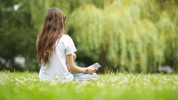 schattig vrouw is lezing tekst bericht Aan mobiel telefoon terwijl zittend in de park. video