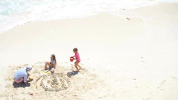 vista de cima para pai e filhas fazendo castelo de areia na praia tropical video