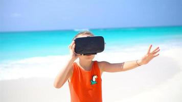 Cute little child girl using VR virtual reality goggles. Adorable girl look into the virtual glasses on white beach video