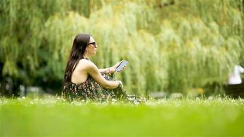 Cute woman is reading text message on mobile phone while sitting in the park. video