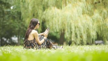 una mujer linda está leyendo un mensaje de texto en el teléfono móvil mientras está sentada en el parque. video