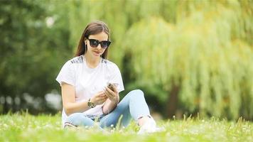 linda mulher está lendo mensagem de texto no celular enquanto está sentado no parque. video