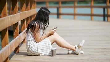 Cute woman is reading text message on mobile phone while sitting in the park. video