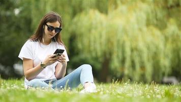 linda mulher está lendo mensagem de texto no celular enquanto está sentado no parque.