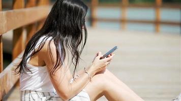 Cute woman is reading text message on mobile phone while sitting in the park. video