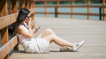 linda mulher está lendo mensagem de texto no celular enquanto está sentado no parque. video