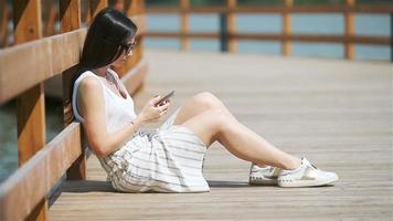 una mujer linda está leyendo un mensaje de texto en el teléfono móvil mientras está sentada en el parque. video