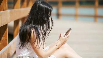 una mujer linda está leyendo un mensaje de texto en el teléfono móvil mientras está sentada en el parque. video