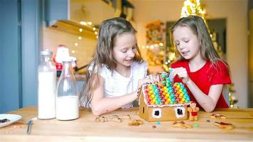 Little girls making Christmas gingerbread house at fireplace in decorated living room. video