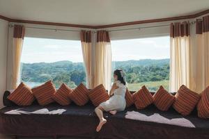 Asian woman relaxing and enjoying the tropical forest view on sofa at panorama room in bright day photo