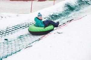 niño divirtiéndose en el tubo de nieve. chico está montando un tubo. entretenimiento de invierno. niño deslizándose cuesta abajo en el tubo foto