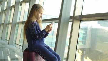 menina adorável no aeroporto perto de grande janela brincando com seu telefone video