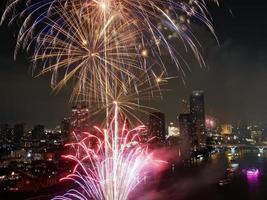 vista de ángulo alto fantástica toma multicolor de larga exposición de fuegos artificiales sobre el río chao phraya, paisaje urbano de bangkok, festival, celebración, feliz año nuevo, arquitectura empresarial. foto