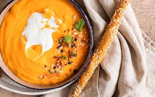 Pumpkin and carrot soup with cream, mint and seeds, brown concrete background. Traditional autumn or winter vegetarian soup with a creamy silky texture. photo