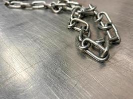 A large iron metal strong powerful shiny chain with links lies on an iron industrial table. Hand-held locksmith tools. The background photo