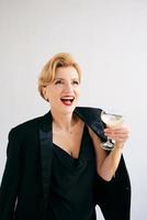 Laughing Caucasian mature stylish elegant woman in tuxedo with glass of sparkling wine. Party, celebration, anti age concept photo