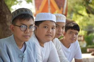Young asian muslim boys sit in a row under the tree in the school park during their free times, soft and selective focus. photo