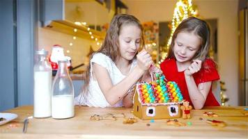 niñas pequeñas haciendo casa de pan de jengibre de navidad en la chimenea en la sala de estar decorada. video