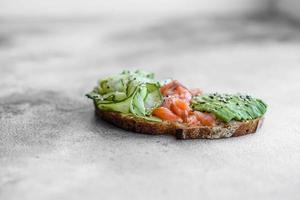 Delicious brown bread toast with salmon, avocado, cucumber and sesame seeds photo