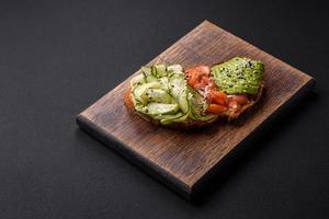 Delicious brown bread toast with salmon, avocado, cucumber and sesame seeds photo