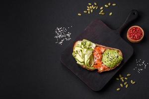 Delicious brown bread toast with salmon, avocado, cucumber and sesame seeds photo